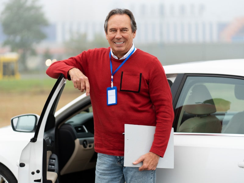 Director de autoescuela posa en la puerta de su coche